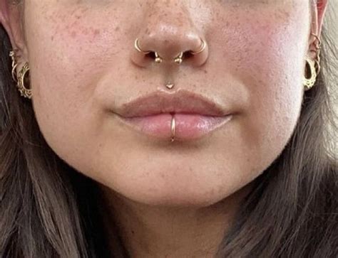 A Close Up Of A Woman With Piercings On Her Nose Wearing Gold Hoop Earrings