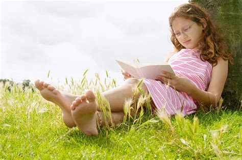 Young Girl Reading A Book While Sitting Under A Tree In The Park