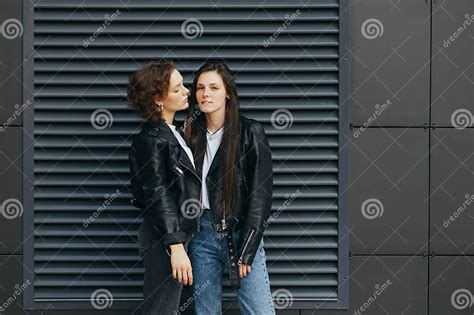 Portrait Of Two Girls In Leather Jackets Standing On A Dark Wall Background And Posing At