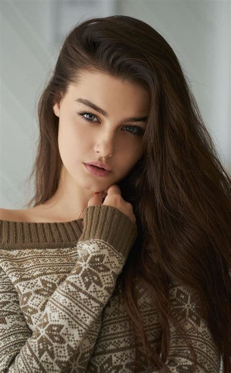 A Woman With Long Brown Hair Is Wearing A Sweater And Has Her Hand On