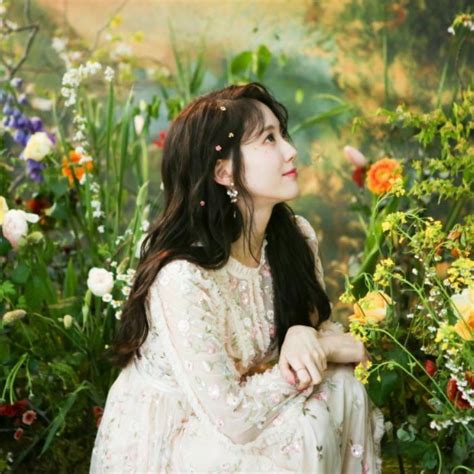 A Woman Sitting In The Middle Of Flowers With Her Hands On Her Knees