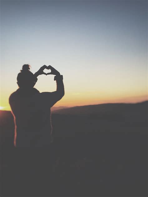 A Silhouette Of A Person Making A Heart Shape With Their Hands Against