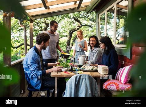 Multi Ethnic Friends Having Food On Porch At Log Cabin During Summer