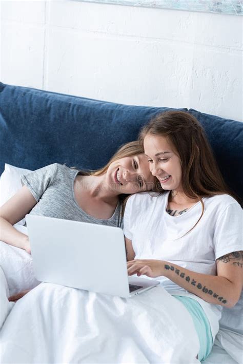 two smiling lesbians embracing while using laptop in bed in morning stock image image of