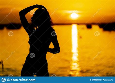 A Lovely Latin Model Is Silhouetted As She Poses With The Rising Sun Behind Her On A Romantic