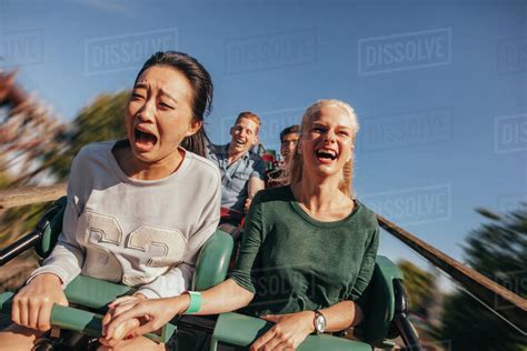 Shot Of Young Friends Cheering And Riding Roller Coaster At Amusement