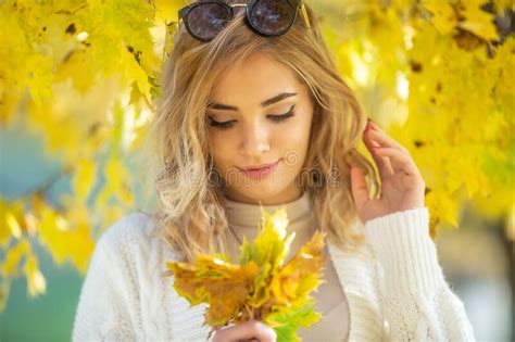 Gorgeous Young Woman Looks Down At Yellow Autumn Leaves In Her Hands