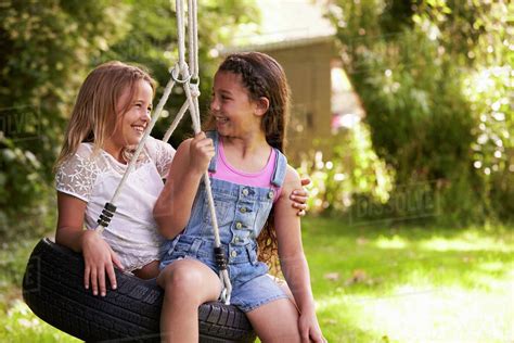 Two Girls Playing Together On Tire Swing In Garden Stock Photo Dissolve