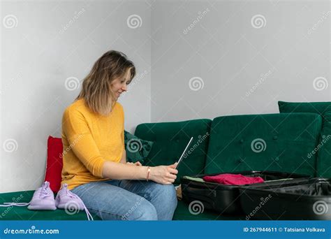 woman put clothes in black suitcase sit on sofa at home room holding tablet happy woman fold