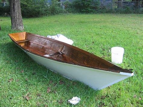 A Small Boat Sitting In The Grass Next To A Tree And Trash Cans On The