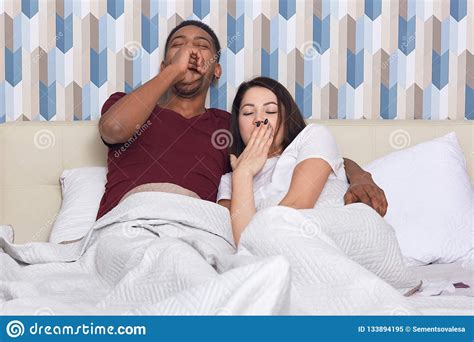 Tired Mixed Race Woman And Man Yawn As Want To Sleep Pose In Bed Against Colourful Wallpapers