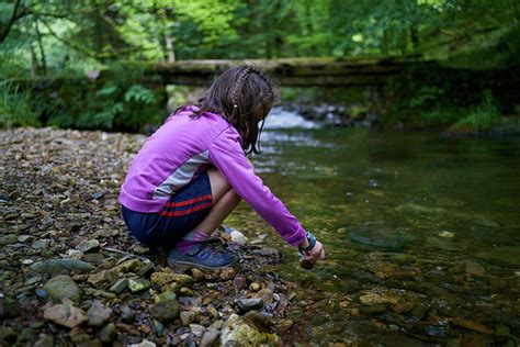 Girl Bending Over A River Bank Playing With Water And Stones Photograph By Cavan Images Fine