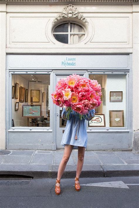 A Woman Is Walking Down The Street With Flowers In Her Hand