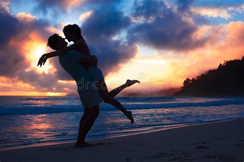 Sunset Silhouette Of Young Couple In Love Hugging At Beach Stock Photo