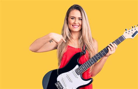 Young Beautiful Blonde Woman Playing Electric Guitar Pointing Finger To