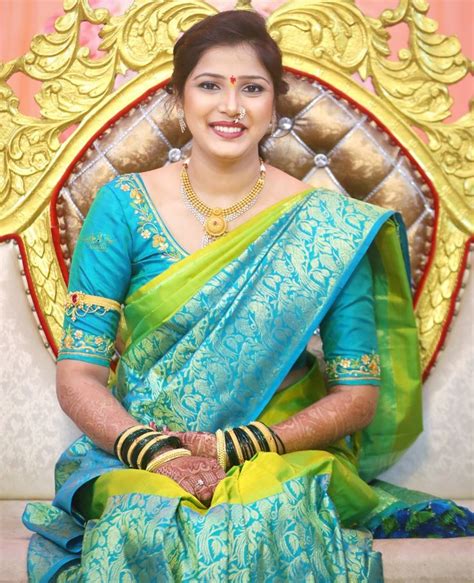 A Woman In A Blue And Green Sari Sitting On A Chair With Her Hands Clasped