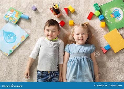 Little Children With Toys And Books Lying On Carpet Indoors Playtime