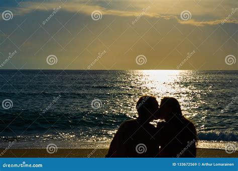 Silhouettes Of A Couple Man And Woman Sitting On A Sandy Beach And