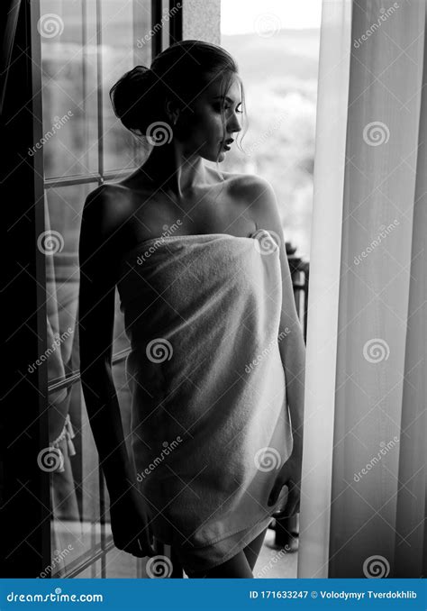 Sensual Young Woman Wrapped In Towel After Having A Shower Standing Near Window And Looking