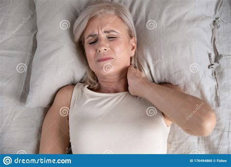 Older Unhappy Woman Lying In Bed Feeling Strong Neck Ache Stock Photo