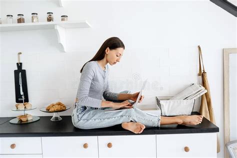 Image Of Cute Brunette Woman Sitting At Kitchen And Using Laptop Stock