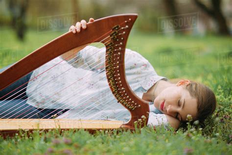 Woman Harpist Lies With Her Harp And Has Enjoy And Relax Among Blooming