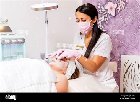 Female Cosmetologist At Protective Mask And Medical Gloves Massages Clients Face Concept Of