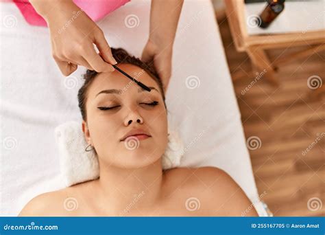 Young Beautiful Hispanic Woman Lying On Table Having Eyebrows Treatment At Beauty Salon Stock
