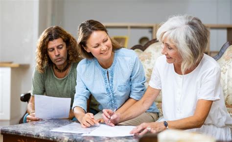 Mature Mother And Adult Children Fill Out Paperwork In Room Stock Photo