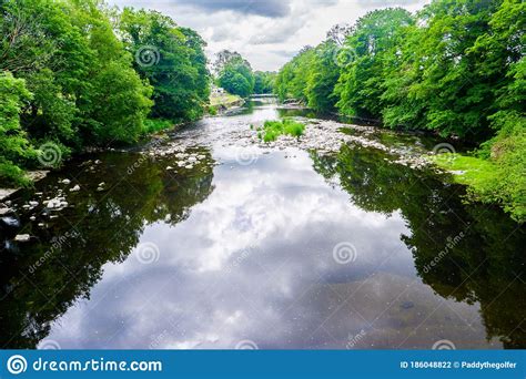 Standing On A Bridge Looking Down A Slow Moving River With Green Banks