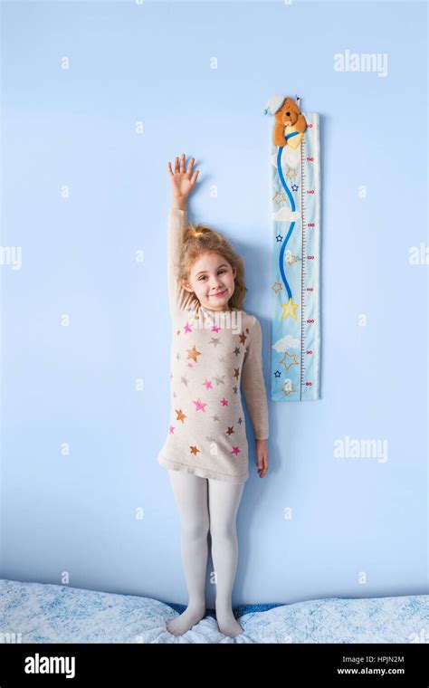 Little Blonde Girl Measuring Height Against Wall In Room Stock Photo