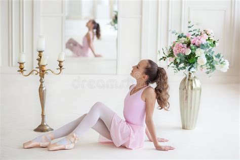 A Cute Little Ballerina In A Pink Ballet Costume And Pointe Sitting On