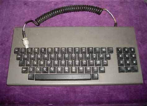 A Computer Keyboard Sitting On Top Of A Purple Blanket With A Cord
