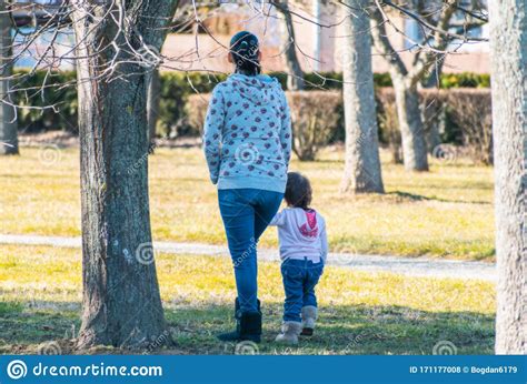 A Mother Walks With The Child Through The Park Holding Her Hand On A