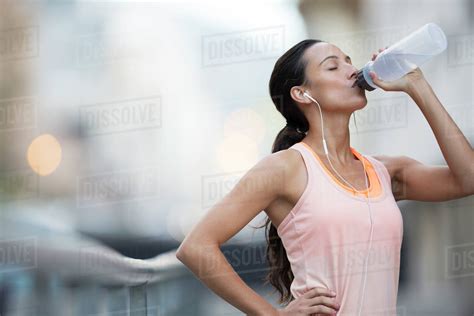 Woman Drinking Water After Exercising On City Street Stock Photo