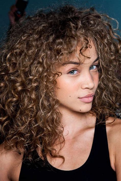 Messy And Voluminous Light Brunette Curly Hair With Darker Roots Highlights And Curly Bangs