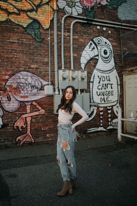 A Woman Standing In Front Of A Brick Wall With Graffiti On It And Her