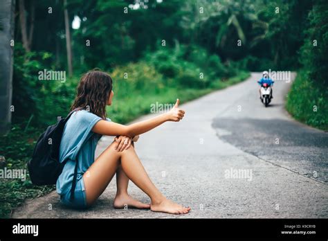 Young Beautiful Woman Hitchhiking Sitting On Road Barefoot Travel