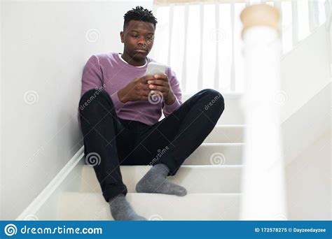 Teenage Boy Being Bullied By Text Message Sitting On Stairs At Home