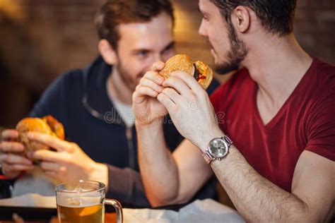 Two Happy Male Friends Eating Tasty Burgers In Bar Stock Photo Image