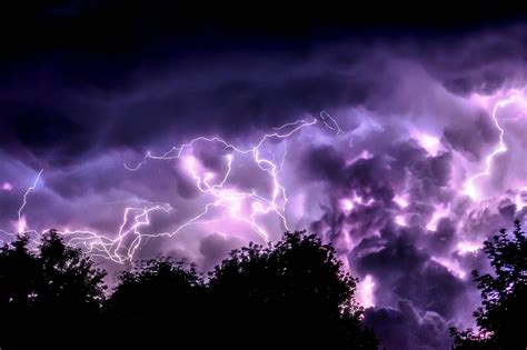 A View Of Purple Lightning And Thunder Bolt In The Sky With Trees In