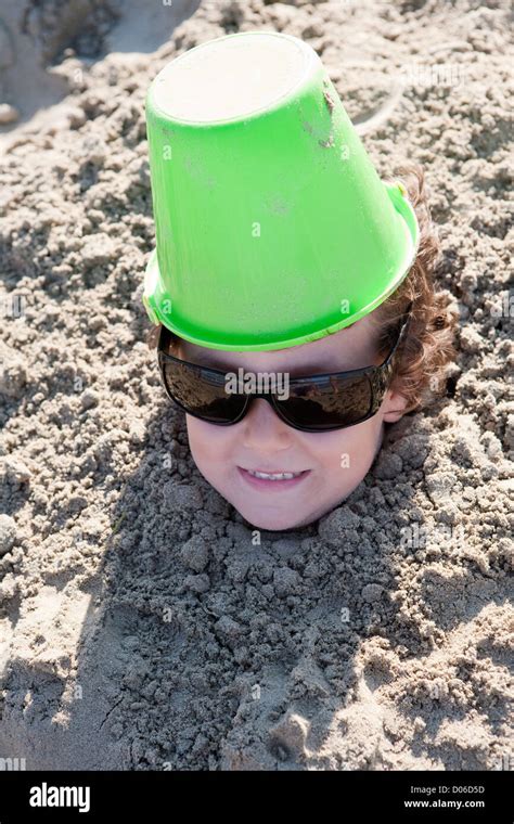 Small Child Buried In The Sand Of The Beach With Sunglasses Stock Photo