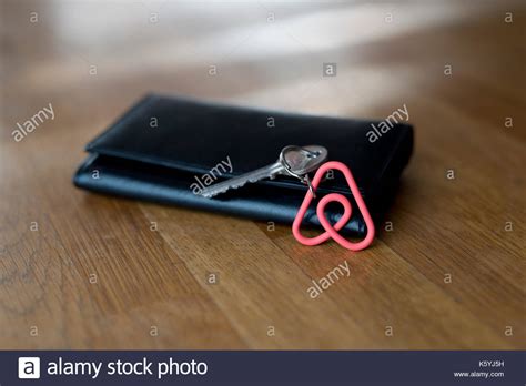 Photo of hand holding phone with airbnb logo on the screen. An Airbnb keyring rests against a wallet on the table top ...