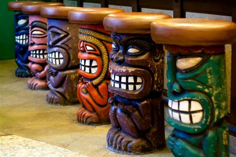Four Tiki Style Stools With Faces Painted On Them In Different Colors