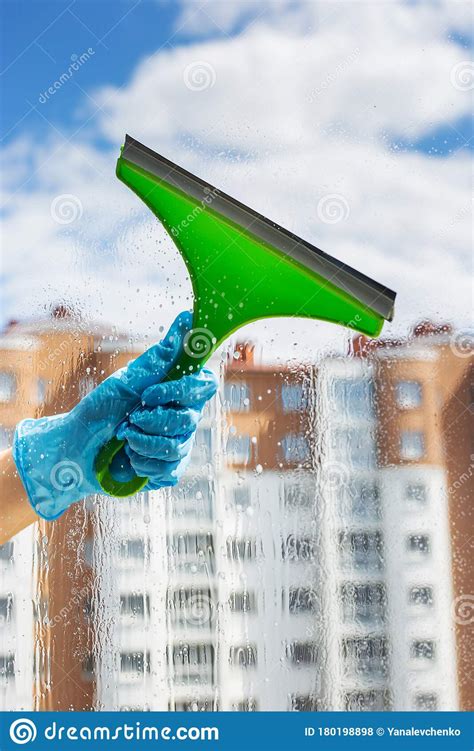 hand cleaning glass window pane with detergent and rubber aluminum wiper a female hands in