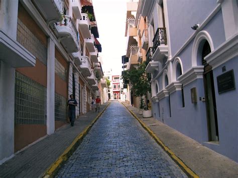 A Man Walking Down An Alley Way In The Middle Of Some Buildings With