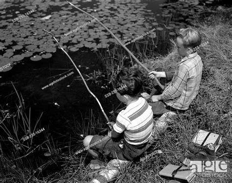 Two Boys Sitting And Fishing With Homemade Fishing Rod Stock Photo