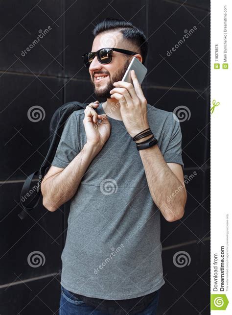 Portrait Of A Beautiful Stylish Guy Hipster With Glasses Talking On The Phone Dressed In A