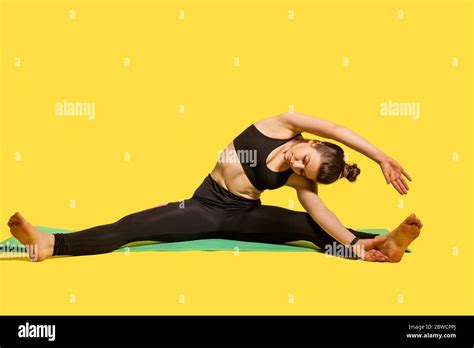 sporty gymnast woman with hair bun in tight sportswear sitting on mat with spread legs bending
