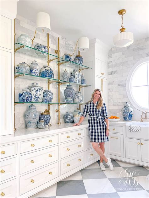 A Woman Standing Next To A Counter With Blue And White Vases On Top Of It
